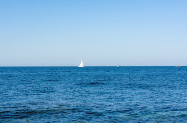 A sailboat cruises on boundless seas. A white sailboat on a blue sea. Classic blue color of the sea