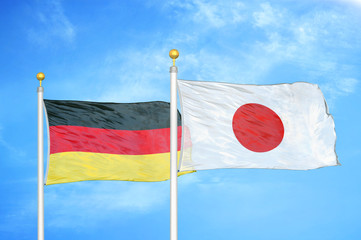 Germany and Japan two flags on flagpoles and blue cloudy sky