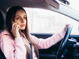 Young girl in pink pite speaks on the phone while sitting in a car.