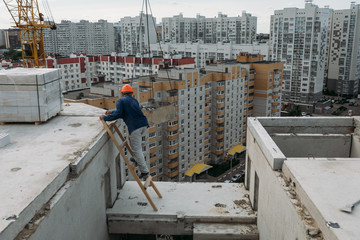 builder on the top floor of a building under construction in the middle of high-rise buildings of a residential area