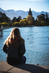 Queenstown, New Zealand, October 6, 2019: Gorgeous image of a blonde girl looking out over the blue lake with the snow capped mountains in the background