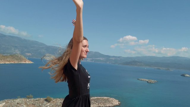 Woman in dress standing on the edge of cliff above sea