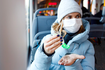 Fototapeta na wymiar Young woman in medical mask looking at side disinfects her hands with tool while sitting on bus near window