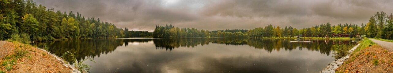 view on a pond from a dyke with forest and dark cloudy sky reflected on water surface