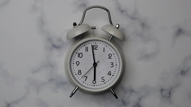Classic Vintage White Alarm Clock With Five Minutes Countdown Before Six Clock And After On An Marble Stone Wall Background.