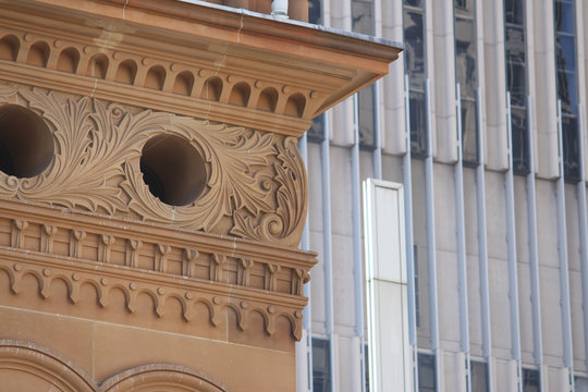 Cityscape with two buildings and a blue sky background. In the foreground is a close up detailing parts of the historic Queen Victoria Building. In the background is a hotel, The Hilton Sydney.