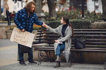 Homeless in a city. Man asking for food. Man with a tablet. Girl helping a homeless