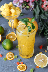 Summer fresh cold drink beverages. Ice Lemonade in the jug and lemons and orange with mint on the table outdoor. Orange lemonade in a glass.