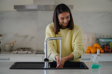 Happy laughing positive girl in a yellow sweater washing hands under the kitchen tab using...
