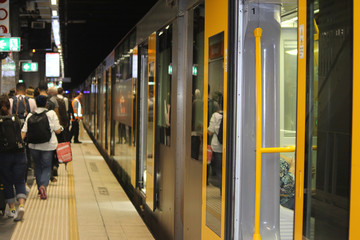 Yellow and grey train with its doors open on a crowded platform in an underground tunnel. Australia