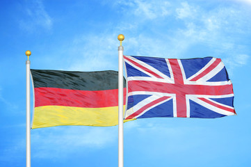 Germany and United Kingdom two flags on flagpoles and blue cloudy sky