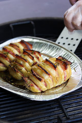 Cooking process. Preparation. Grilled potatoes with bacon and spices in a foil plate with hands of chef and cooking spatula. Summer, picnic. Background image, copy space