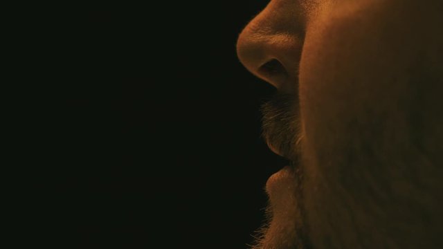 Close up of a man's mouth as he sneezes with a black background and sickly yellow lighting.
