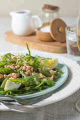 Arugula and trout salad with egg and asparagus on a plate on a table covered with a tablecloth with a glass of wine and a glass of water. Vertical arrangement