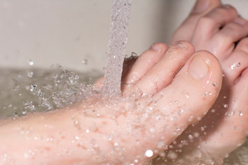 Women's feet under the tap water, drops. The adoption of water treatments in the bathroom.