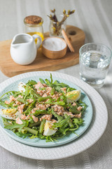 Arugula and trout salad with egg and asparagus on a plate on a table covered with a tablecloth and a glass of water vertical arrangement