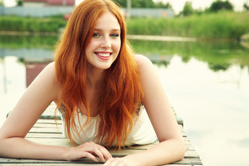 summer portrait of a young redhead woman on background of water in countryside.