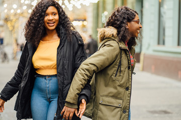 Portrait of two nigerian black women outdoor having fun hugging riding piggyback in cold weather. Two female student enjoying holiday in street. Happiness, fooling around, togetherness concept