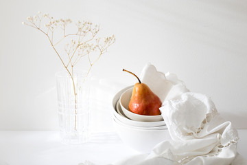 Still life with yellow-red pear Duchess in pile of bowls and a white embroidered napkin