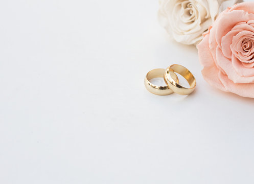 Golden wedding rings and two roses in soft tones on white background