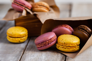 Assortment of delicious traditional french macaroons. Colorful sweet dessert. Lemon, chocolate, caramel, raspberry flavors. Wooden rustic background, craft paper, close up, macro
