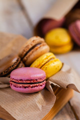 Assortment of delicious traditional french macaroons. Colorful sweet dessert for real gourmands. Lemon, chocolate, caramel, raspberry flavors. Wooden rustic background, craft paper, close up, macro
