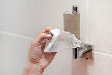 Hand of caucasian woman in the toilet taking the last piece of paper from the roll. Last piece of...