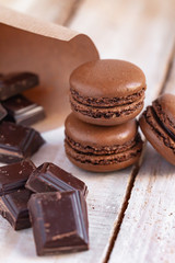 Delicious traditional french macaroons. Sweet dessert for real gourmands. Chocolate and caramel flavor. Pieces of dark chocolate to illustrate ingredients. Wooden background, close up, macro