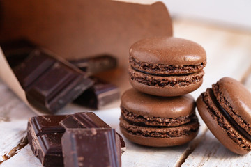 Delicious traditional french macaroons. Sweet dessert for real gourmands. Chocolate and caramel flavor. Pieces of dark chocolate to illustrate ingredients. Wooden background, close up, macro