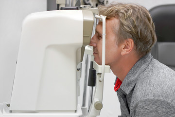 Male checks his vision on the machine checking patient vision at eye clinic or optics store. Face closeup.