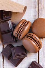 Delicious traditional french macaroons. Sweet dessert for real gourmands. Chocolate and caramel flavor. Pieces of dark chocolate. Wooden background, close up, macro, flat lay top view