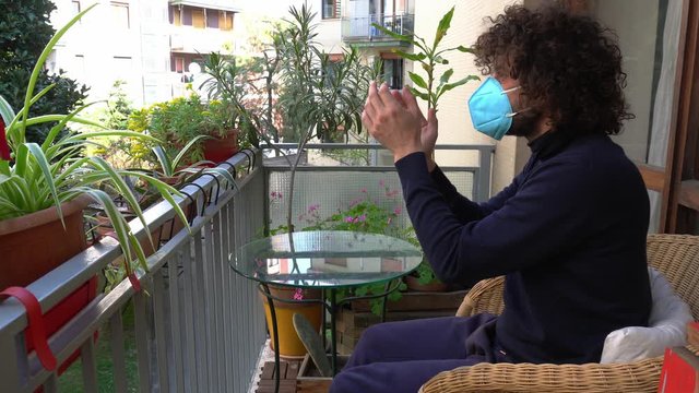 Europa, Italy , Milan - Man 40 years old with mask in quarantine at home - Smart work in apartment 
applauds the neighbors who made a musical flash mob on the balcony