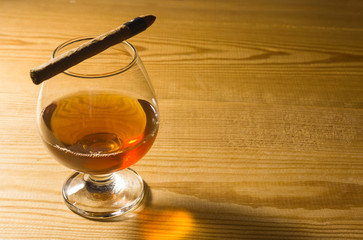Glass glass with cognac on a wooden table and a cigar on the glass. Free space for text on the side.