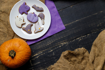 Pumpkin and Halloween cookies on white plate, sackcloth on black wooden background. Hallooween trick or treat concept. Copy space.