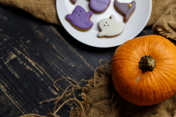 Fototapeta na wymiar Pumpkin and Halloween cookies on white plate, sackcloth on black wooden background. Hallooween trick or treat concept. Copy space.