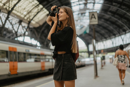 Blonde woman with a smile on her face uses her camera to take pictures of the roof of the train station, she is a tourist who visits different cities and takes photos of different urban views.