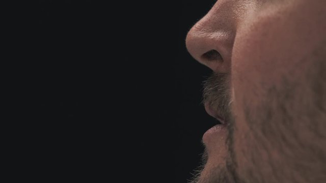 Close up of a man's mouth as he sneezes with a black background and neutral lighting.