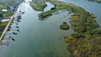 Aerial view of Thu Bon river, green islands on water, long tail fishing boats moored to shore. Hoi An, Vietnam