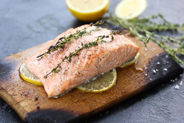 Grilled salmon with thyme, lemon, salt and spices on a wooden board on a black background. Baked red fish, trout. Background image, copy space