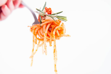 Spaghetti bolognese sprinkled with cheese and decorated with a rosemary twig on a fork held by a hand on a white background
