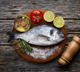 Dorado fish on the wooden  with lime, rosemary, tomato, oil  and salt. Top view.