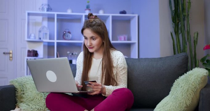 Woman connecting with a laptop and doing online shopping using a credit card. Young girl are buying online with credit card while sitting on sofa. Woman are using laptop and doing online transactions.