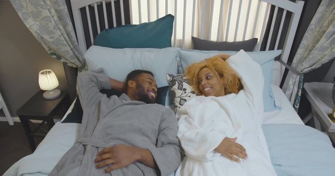 Happy african couple in bathrobes resting on bed at home
