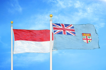Indonesia and Fiji two flags on flagpoles and blue cloudy sky
