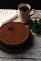 chocolate cheesecake, on a wooden rustic backdrop, cup of coffee on background, black background