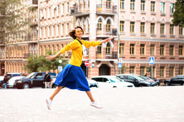 Young beautiful woman in long yellow sweater and blue skirt walking in cozy city street.Full-length portrait of trendy stylish girl in the city.