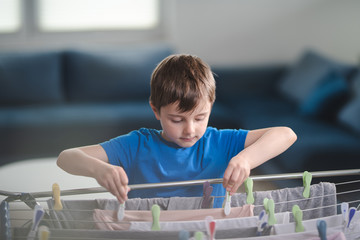 Caucasian little boy helping with household activities, hooking clothes with pinch