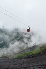 Bright red cabin of the old ski lift surfes through the clouds