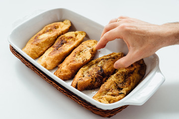 Male hand taking torrijas, typical Spanish sweet fried toasts of sliced bread soaked in eggs and milk on tray isolated on white background