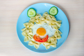 Child food. Funny food. Plate with pasta with fried egg and vegetables in the form of funny face. Children's menu and lunch concept. Flat lay, top view.